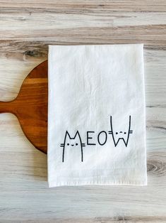 a tea towel with the word meow printed on it and a wooden spoon sitting next to it