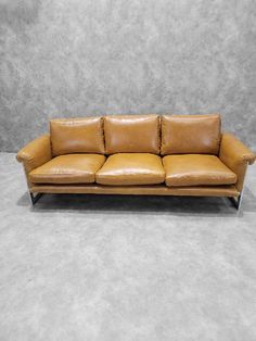 a tan leather couch with two pillows on it's back and the seat upholstered