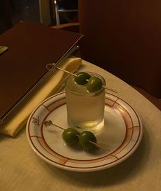 a glass with some olives on a plate next to a book and an open notebook