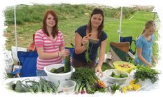 two women standing in front of a table full of vegetables