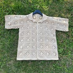 a crocheted sweater laying on the grass with a coat hanging from it's collar