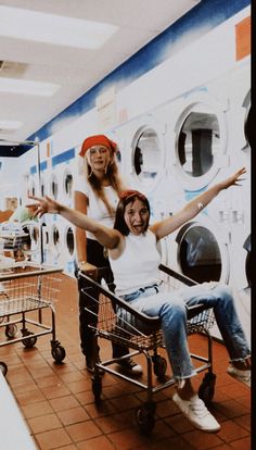 two women sitting in a shopping cart with their arms outstretched