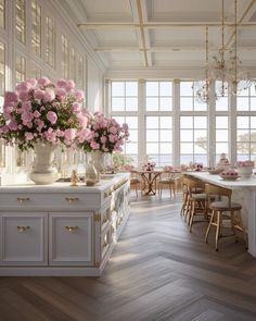 a kitchen with white cabinets and pink flowers in vases on the counter top next to an island