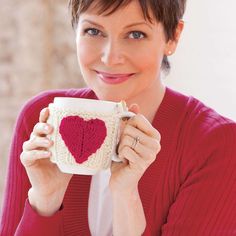 a woman holding a coffee cup with a knitted heart on it