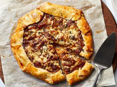 a pizza sitting on top of a wooden cutting board next to a knife and fork