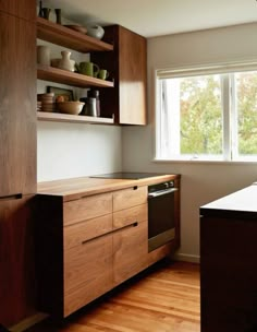 an empty kitchen with wooden cabinets and white dishes on the counter top, near a window