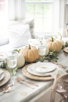 the table is set with white pumpkins and dishes