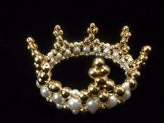 a gold and white beaded crown brooch with pearls on it's sides