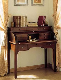 a wooden desk with books on it in front of two framed pictures and window curtains