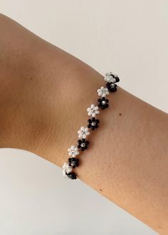 a woman's arm wearing a bracelet with black and white beaded flowers on it