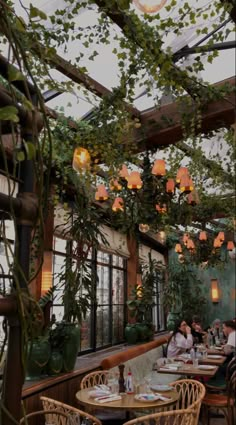 people sitting at tables in a restaurant with plants hanging from the ceiling