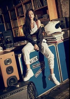 a woman sitting on top of a blue box next to bookshelves and speakers