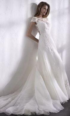 a woman in a white wedding dress standing against a wall with her hands on her hips