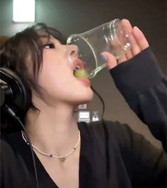 a woman drinking water from a glass with headphones on