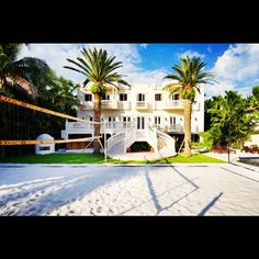 a beach volleyball court in front of a large white building with balconies and palm trees