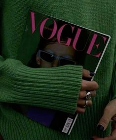 a woman in green sweater holding a magazine with her face partially hidden by her hands