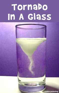 a glass filled with liquid sitting on top of a table next to a purple wall