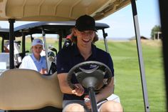 a man driving a golf cart on a green field with people in the back ground