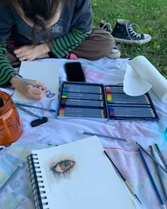 a woman sitting on the ground with some art supplies in front of her and an open notebook