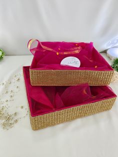 two pink boxes with gold trims on white cloth and beaded decorations in background