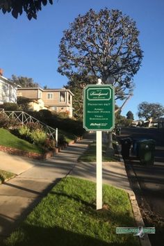 a green sign on the side of a road in front of some houses and trees