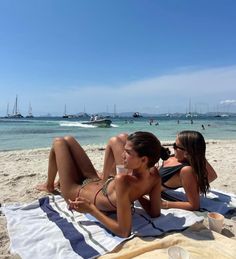 two women are laying on the beach drinking coffee