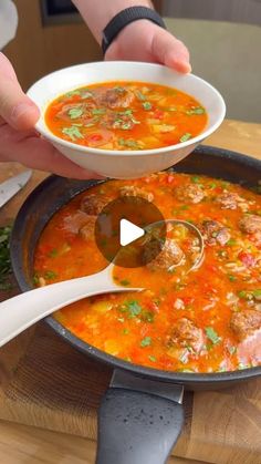 a person is holding a spoon over a bowl of soup