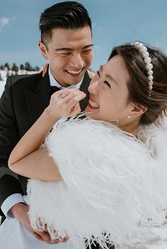 a bride and groom smile at each other while they stand in the snow with their arms around each other