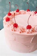 a cake with pink frosting and cherries on top, sitting on a table