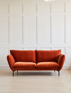 an orange couch sitting on top of a hard wood floor next to a white wall