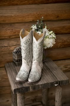 a pair of white cowboy boots sitting on top of a wooden bench next to flowers