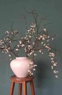 a white vase sitting on top of a wooden stand next to a wall with flowers in it