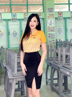 a woman standing in front of desks wearing a skirt and yellow shirt with black heels