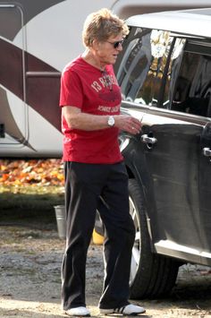 an older woman standing next to a parked car in front of a camper trailer