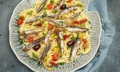 a white plate topped with pasta and sardines on top of a blue towel