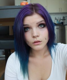 a woman with blue hair and piercings on her nose is posing for the camera