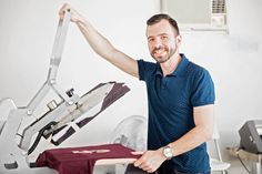 a man standing next to an ironing machine with his arm up in the air