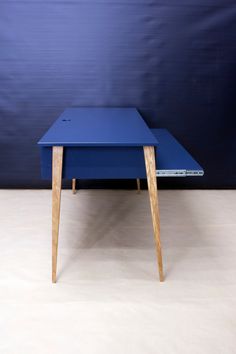 a blue table sitting on top of a white floor next to a blue wall and wooden legs