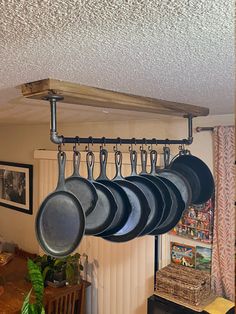 pots and pans are hanging from a rack on the ceiling above a table in a kitchen