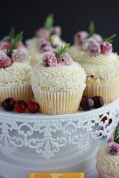 cupcakes with white frosting and cranberries are on a cake plate