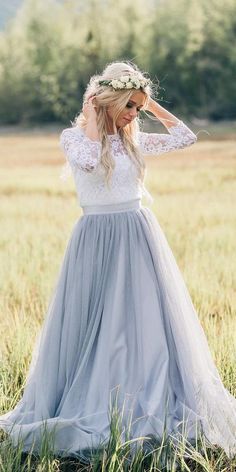 a woman standing in a field wearing a dress with long sleeves and a flower crown on her head