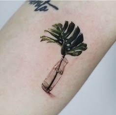 a small palm tree in a bottle tattoo on the right arm and shoulder, with writing underneath it