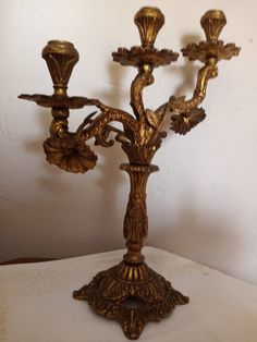 a golden candelabra with four candles on it's stand, against a white wall