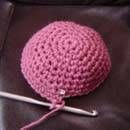 a pink crocheted ball on top of a black leather chair with a knitting needle