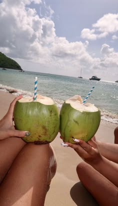 two people sitting on the beach holding up coconuts