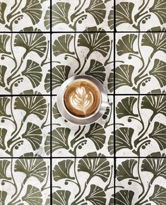 a cup of coffee sitting on top of a tiled counter next to a plate with an art nouveau design