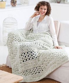 a woman is sitting on a couch with a crocheted blanket