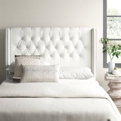 a white bed sitting next to a window with lots of pillows on top of it