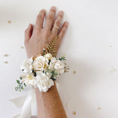 a woman's hand wearing a bracelet with white flowers and greenery on it