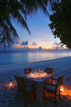 a dinner table set up on the beach with candles in front of it at sunset